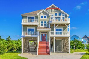 A multi-story beachfront property with a covered entrance, multiple balconies, and a red staircase leading to the main entrance.