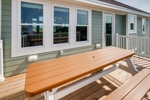 Una terraza de madera con un banco, una barandilla y una casa de tres ventanas.