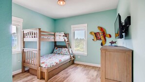 Un lit superposé pour enfants avec une échelle, une armoire en bois et un téléviseur fixé au mur.