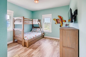 Ein Kinderstockbett mit einer Leiter, einem Holzschrank und einem an der Wand befestigten Fernseher.