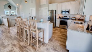 Une cuisine moderne avec des meubles blancs, des appareils en acier inoxydable et un îlot central en bois doté de tabourets de bar.