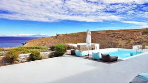 A pool area with a view of the sea and a hill in the background.