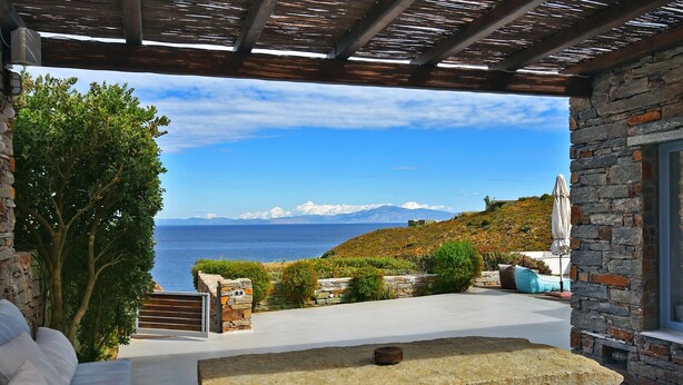 A stone-walled outdoor seating area with a view of the sea and mountains.
