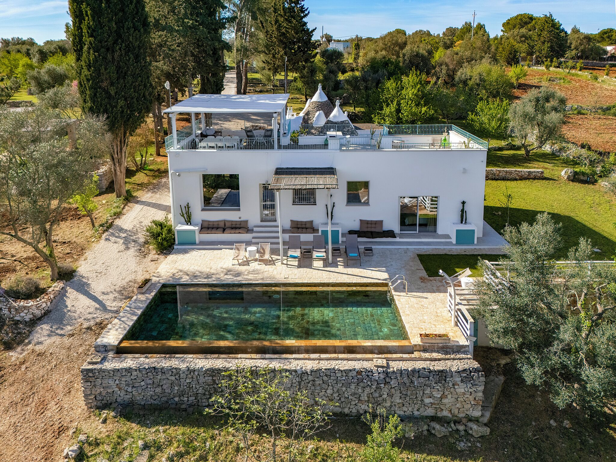 Une villa moderne dotée d’une piscine, d’un espace extérieur aménagé et d’un mur en pierre qui entoure la zone de la piscine.
