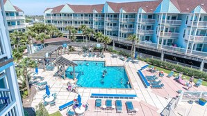 A hotel with a central pool surrounded by lounge chairs and umbrellas, multiple balconies, and a view of the ocean. - Great Views! Heated Pools, Hot Tubs & Easy Beach Access (Galveston)