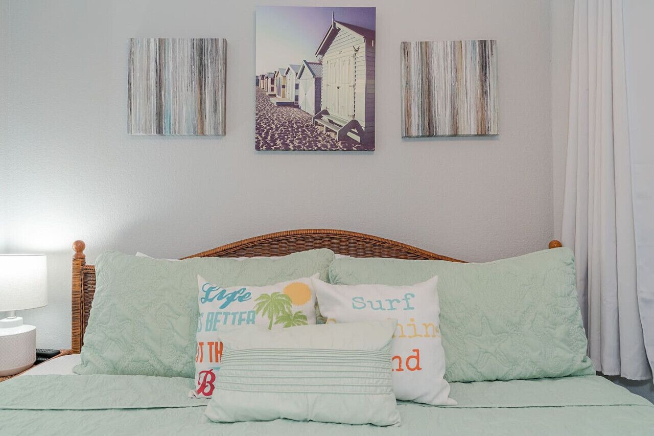 A bedroom with a bed, pillows, a lamp, and artwork on the wall.