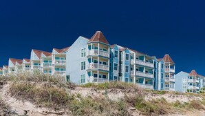 A beachfront hotel with multiple balconies, a prominent corner tower, and a sandy foreground. - Great Views! Heated Pools, Hot Tubs & Easy Beach Access (Galveston)