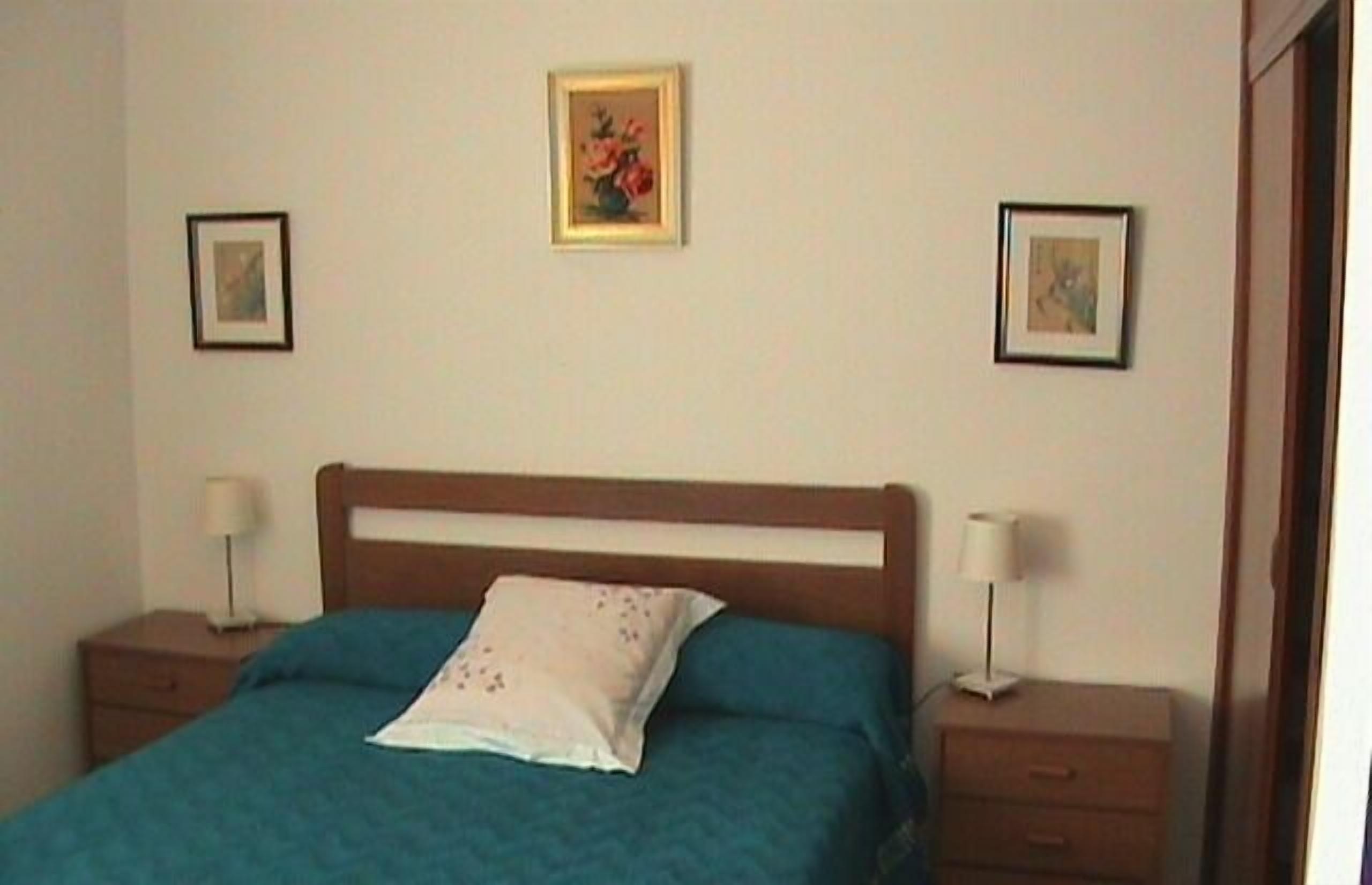 Un dormitorio con una cama individual, dos mesitas de noche y dos cuadros en la pared.