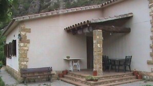 A building with a stone facade, a covered patio area with a table and chairs, and a bench outside. - Rural apartment Racó de les Heures for 8 people (Arbolí)