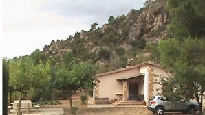 A small building with a stone facade, a car parked in front, and a hilly landscape in the background. - Rural apartment Racó de les Heures for 8 people (Arbolí)