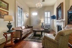 A living room with a brown leather sofa, a round coffee table, patterned armchairs, a chandelier, and a fireplace. - Prime Location just steps from the French Quarter & 3 Blocks to Bourbon St, (New Orleans)