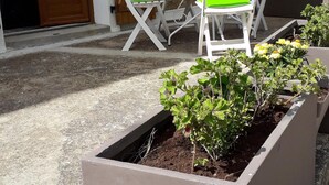 A patio area with a table and chairs, a yellow umbrella, and flower planters. - T2 any comfort in house of village (Grossa)