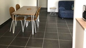 A modern living space with a dining area featuring a wooden table and chairs, a sofa, and two wall-mounted light fixtures. - T2 any comfort in house of village (Grossa)