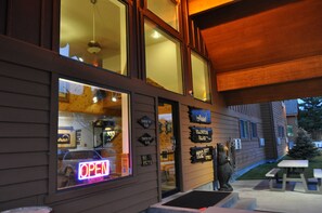 A wooden building with large windows, a neon 'OPEN' sign, and a bear statue.