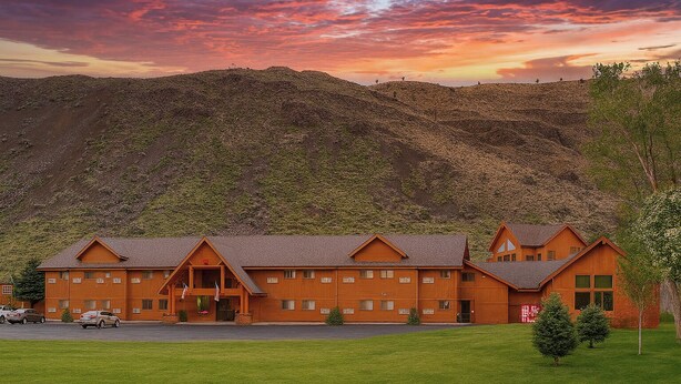 A large wooden lodge with multiple rooms, a parking area, and a view of a mountainous landscape. - Yellowstone Village Inn and Suites (Gardiner)