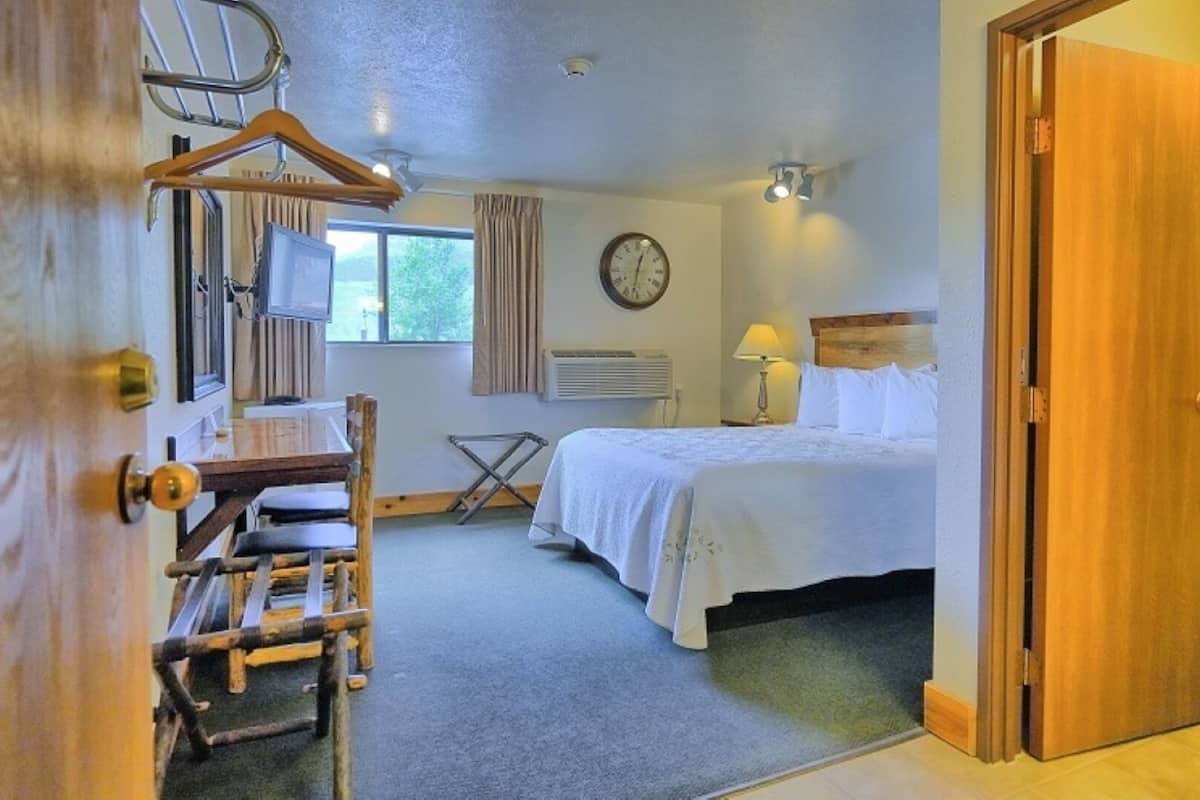 A hotel room with a bed, a desk, a chair, a clock, and a window.
