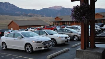 A parking lot with several cars, a building with a wooden facade, and mountains in the background.