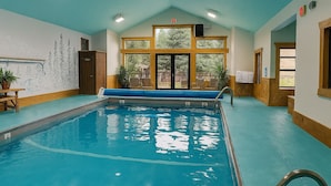 An indoor swimming pool with a wooden deck, a mural of trees, and a view of the outdoors. - Yellowstone Village Inn and Suites (Gardiner)