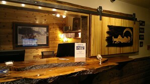 A wooden reception desk with a framed picture of a snowy landscape, a clock, and a welcome sign. - Yellowstone Village Inn and Suites (Gardiner)