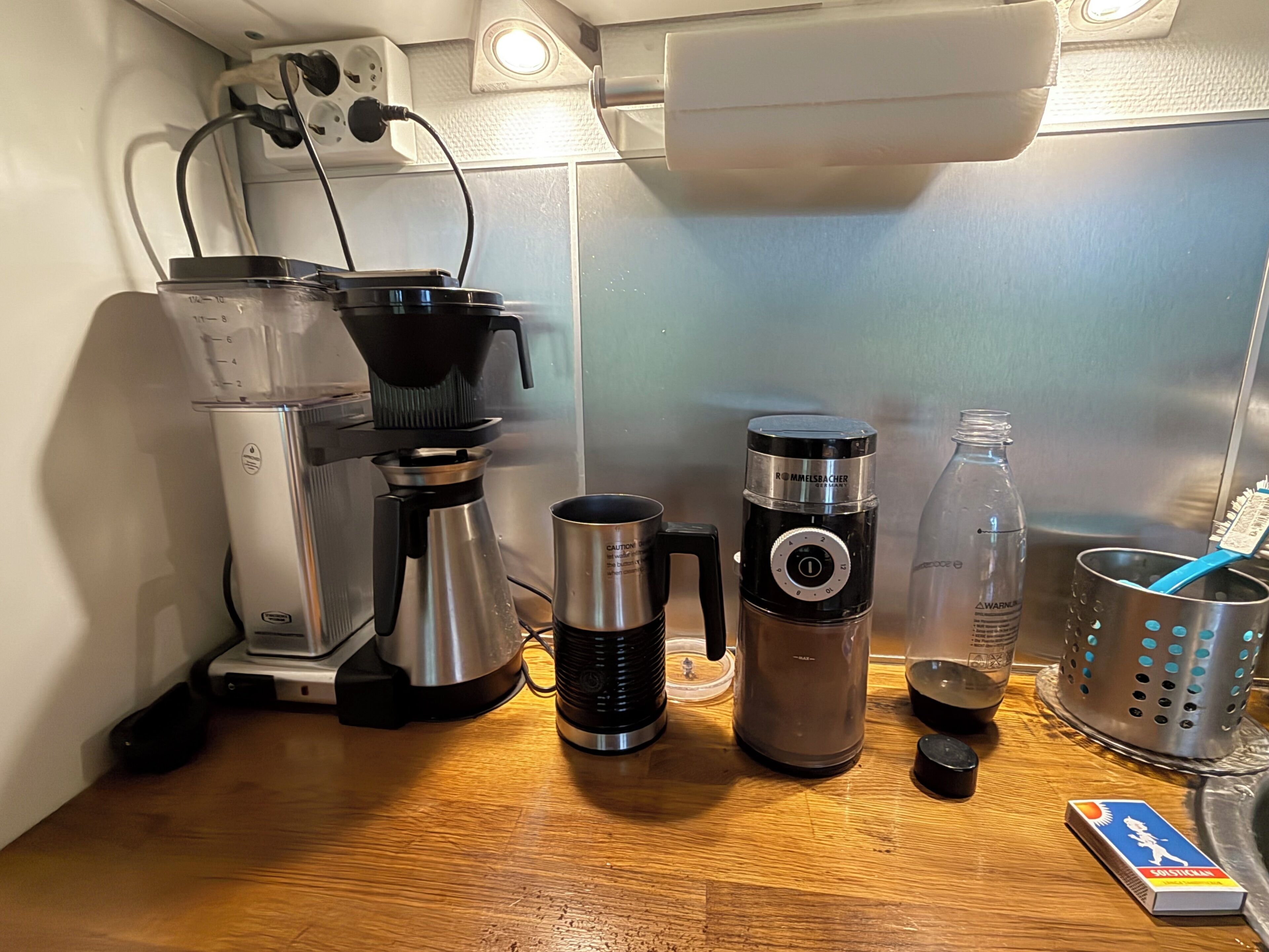 Un comptoir de cuisine avec une machine à café, un thermos, une bouteille d’eau, une bouilloire et un jeu de cartes.