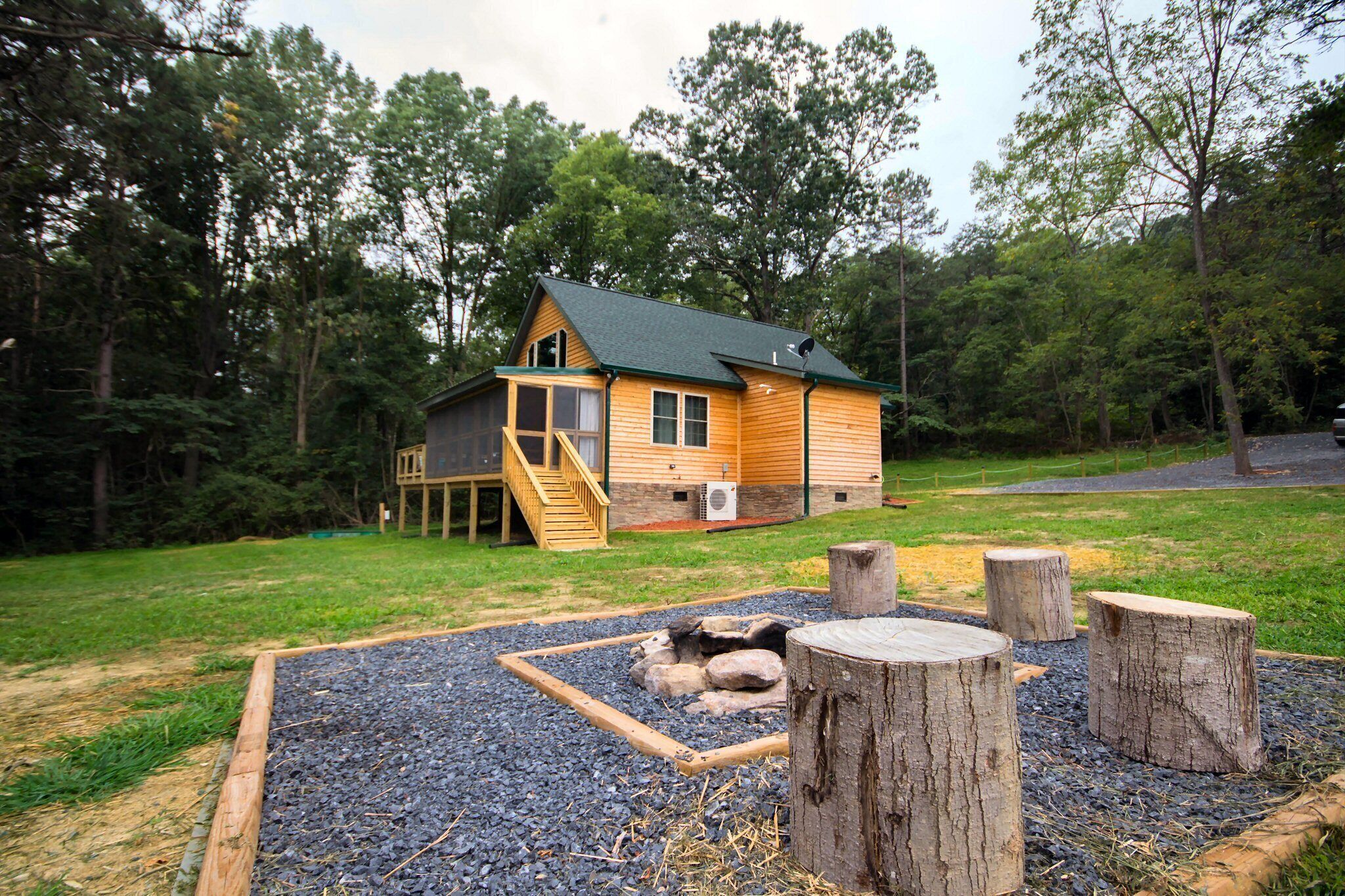 Une cabane en bois dotée d’une terrasse, entourée d’une zone recouverte de gravier, avec des poteaux en bois et un petit jardin de rocaille.