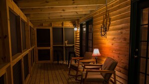 A wooden cabin with a porch, furnished with chairs and a table, and a door with a window.