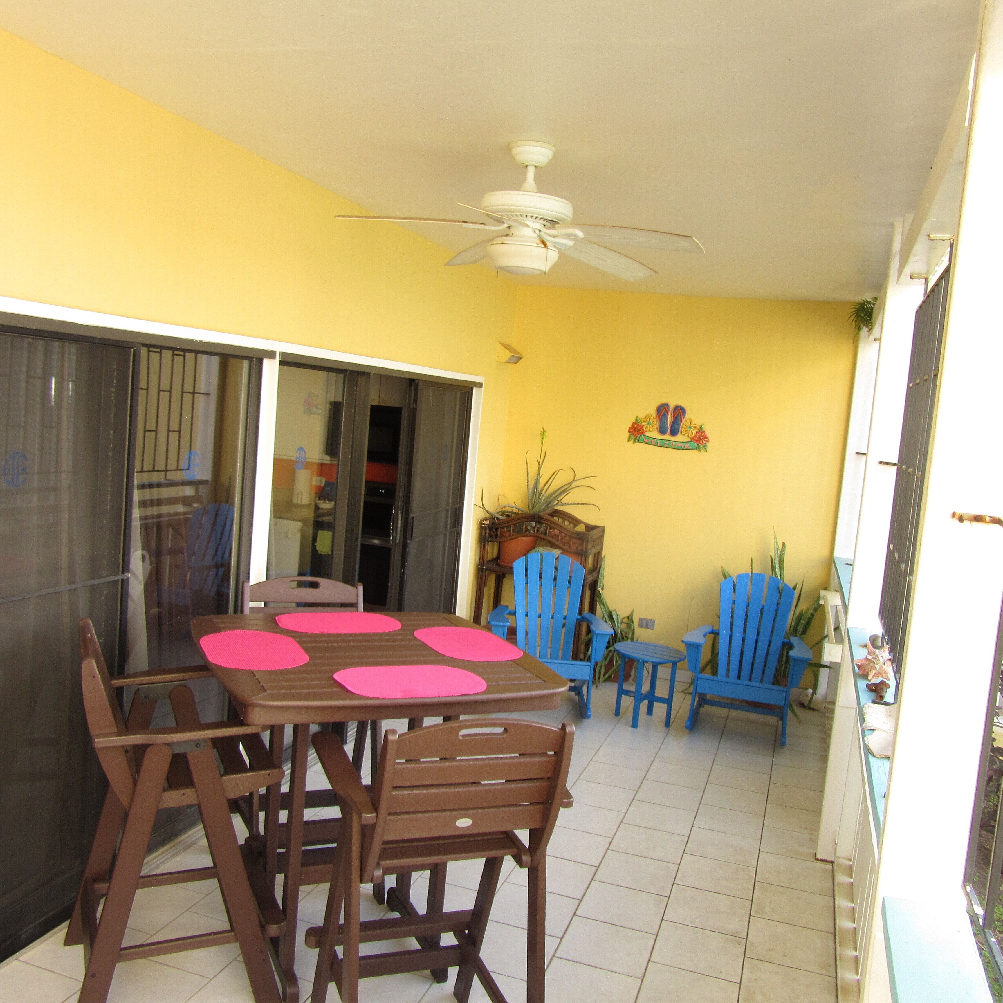 A dining area with a table and chairs, a ceiling fan, and a yellow wall with a welcome sign.