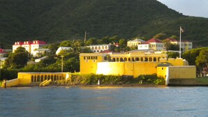 A coastal town with a prominent yellow building, a flagpole, and a hill in the background. - No Shirt, No Shoes, No Steps.  Visit Easy Street In St. Croix! (Christiansted)