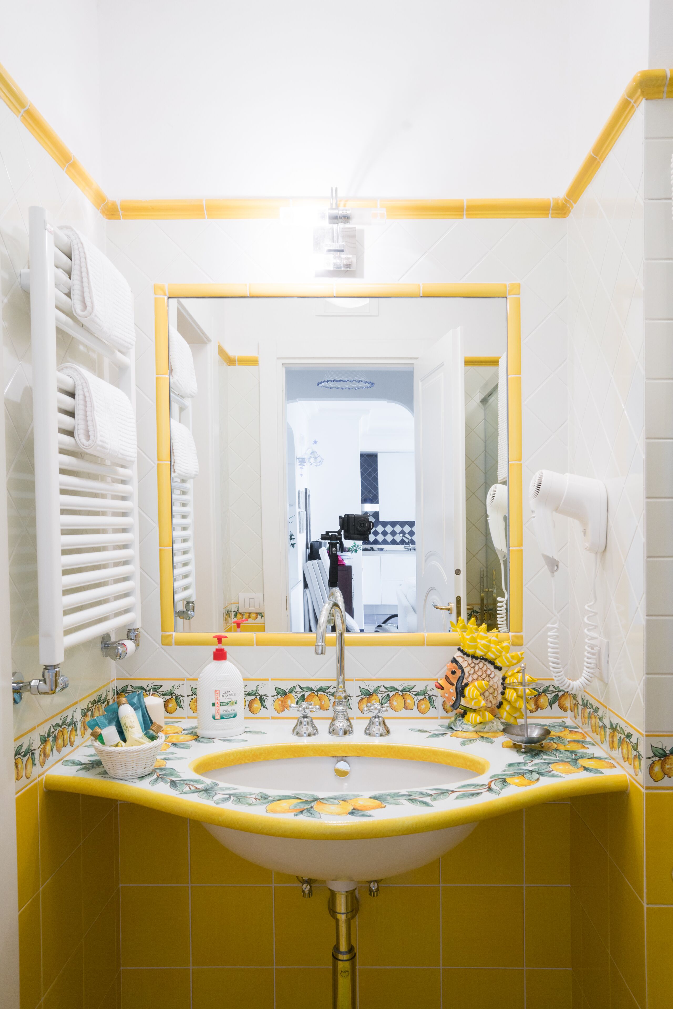 A bathroom with a yellow-tiled sink, a mirror, a towel rack, and a hairdryer.