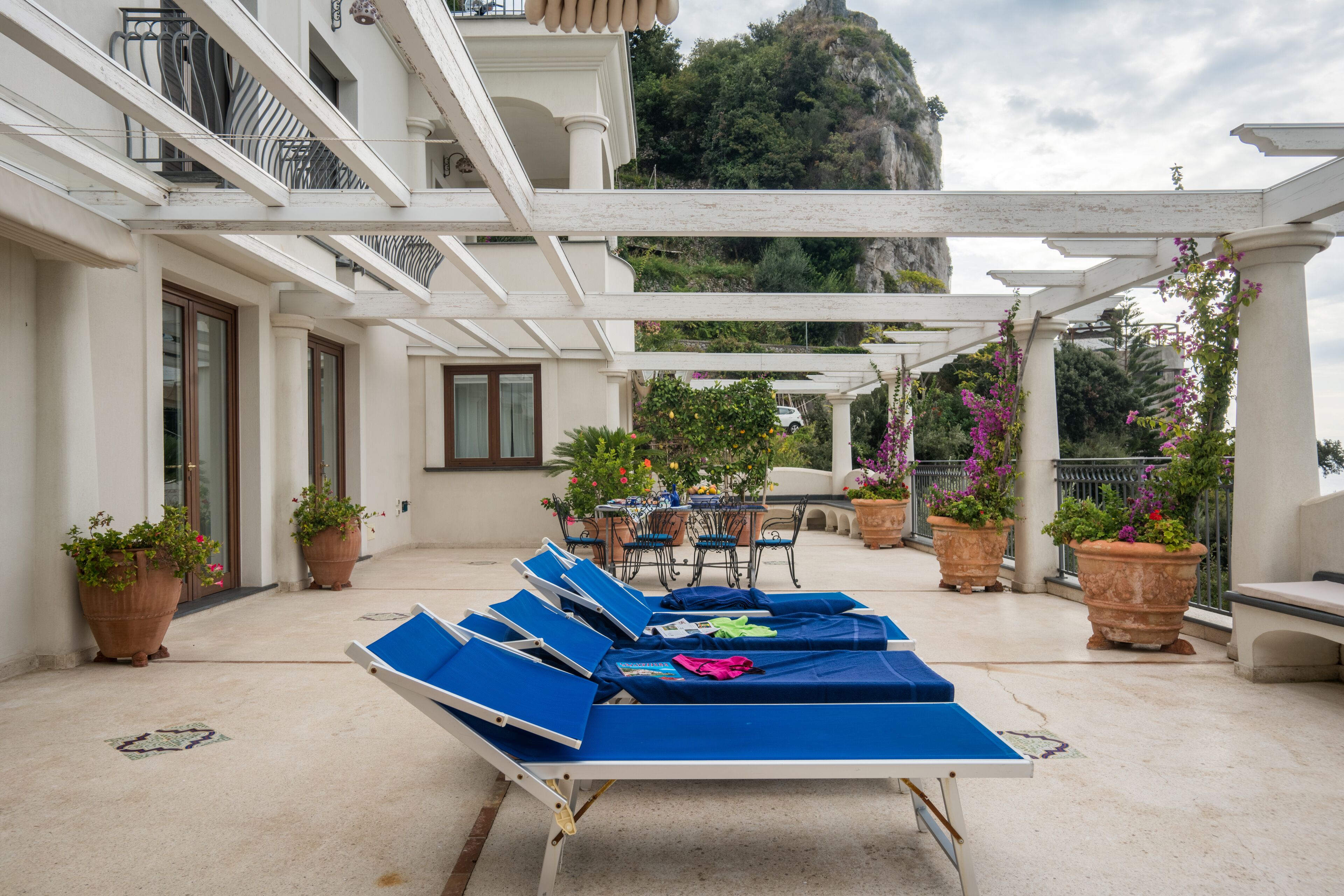 A covered outdoor seating area with lounge chairs, a table, and potted plants.