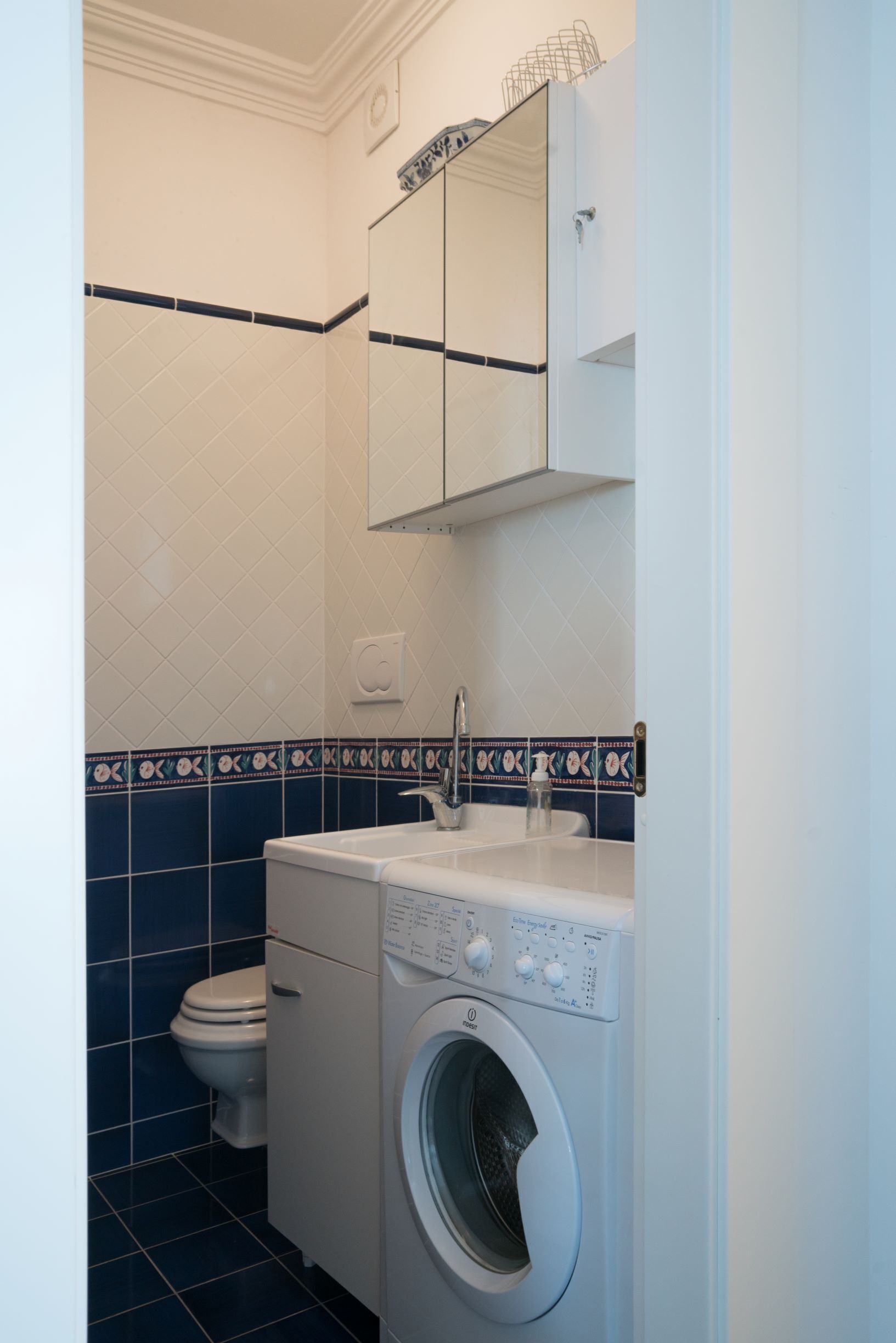 A compact bathroom with a washing machine, toilet, and a mirror above the sink.