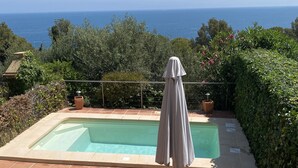 Ein Schwimmbad mit Meerblick, umgeben von viel Grün und einer gefliesten Terrasse mit Tisch und Stühlen.