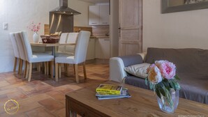 A modern living room with a dining area, a sofa, a coffee table with books, and a vase with flowers. - Mazet de La Tour - private terrace and shared swimming pool -Vallée des Baux (Paradou)