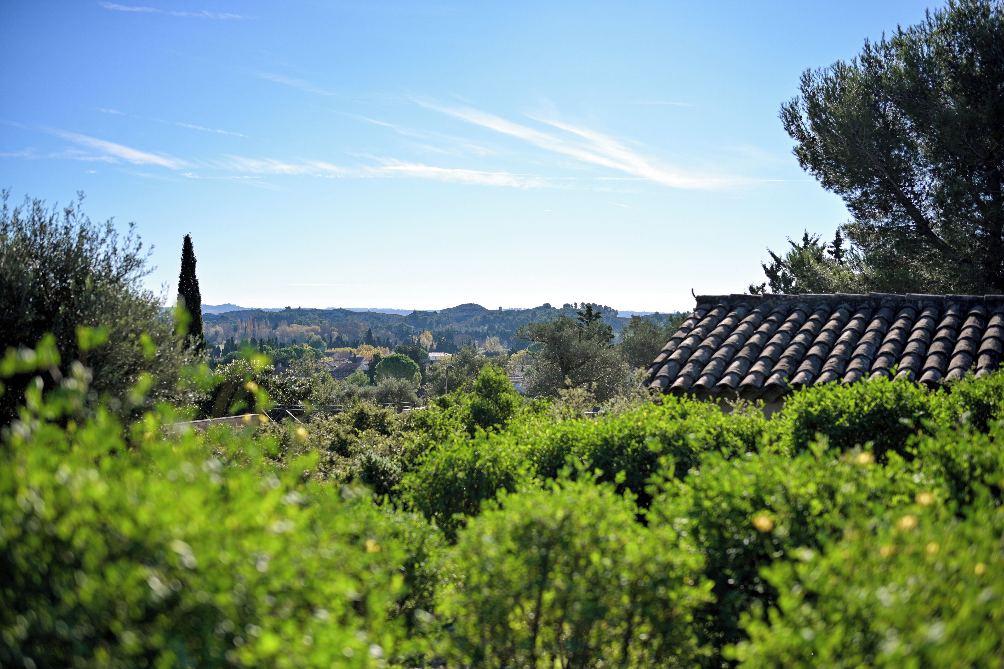 A view of a rural landscape with a tiled roof house, surrounded by greenery and hills in the distance.