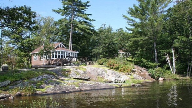 A lakeside cabin with a dock, surrounded by dense forest and a calm lake.
