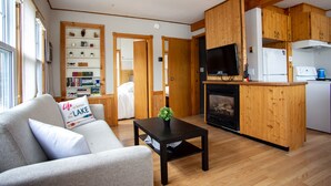 A cozy living room with a sofa, a coffee table, and a fireplace. There is a kitchen area with wooden cabinets and a television.