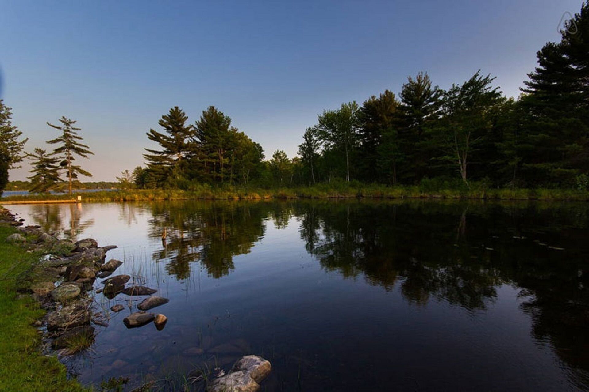 Un lac paisible où se reflètent les arbres et où le ciel est dégagé.