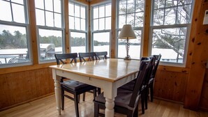 A wooden-paneled room with a large table and chairs, large windows, and a lamp.
