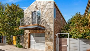 Une maison moderne à deux étages, dotée d’une façade en pierre, d’un balcon et d’un garage.