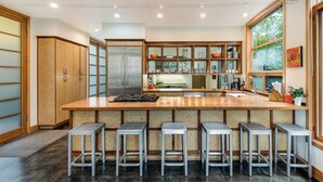 Une cuisine moderne dotée d’un îlot central, de tabourets de bar, d’appareils électroménagers en acier inoxydable et d’une grande fenêtre.