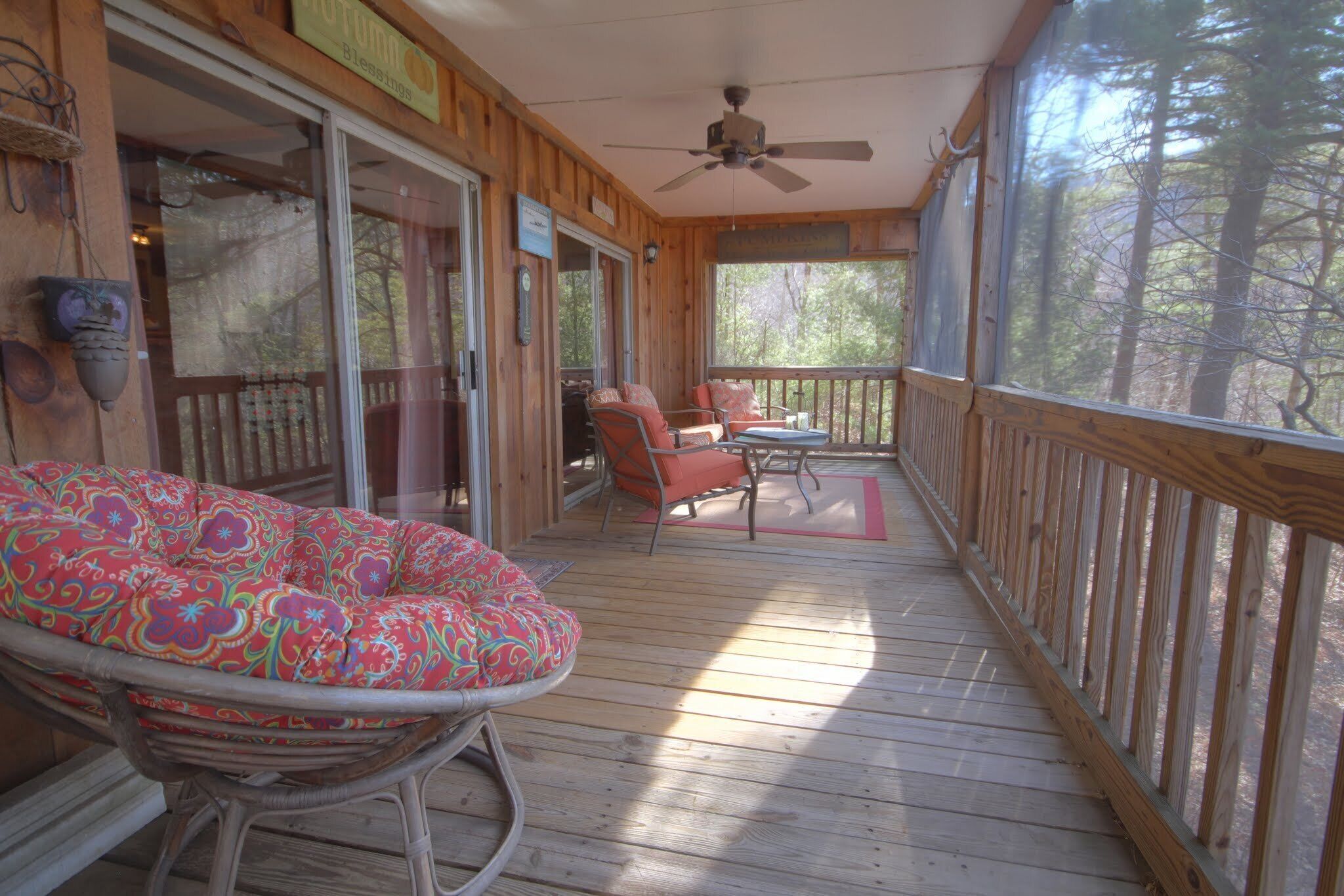 A wooden deck with a ceiling fan, wicker chairs, and a cushioned bench.