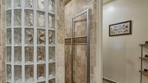 A bathroom with a glass shower enclosure, a marble wall, and a framed artwork on the wall.