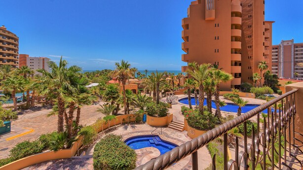 A resort with multiple swimming pools, palm trees, and a large building with balconies.