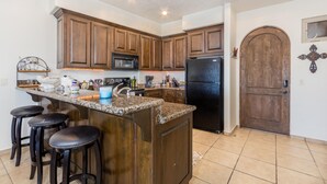 A kitchen with wooden cabinets, a black refrigerator, a microwave, and a granite countertop.