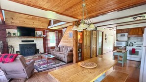 Ein Holzinnenraum mit Kamin, Sofa, Couchtisch, Esstisch, Küchenbereich und einer Treppe.