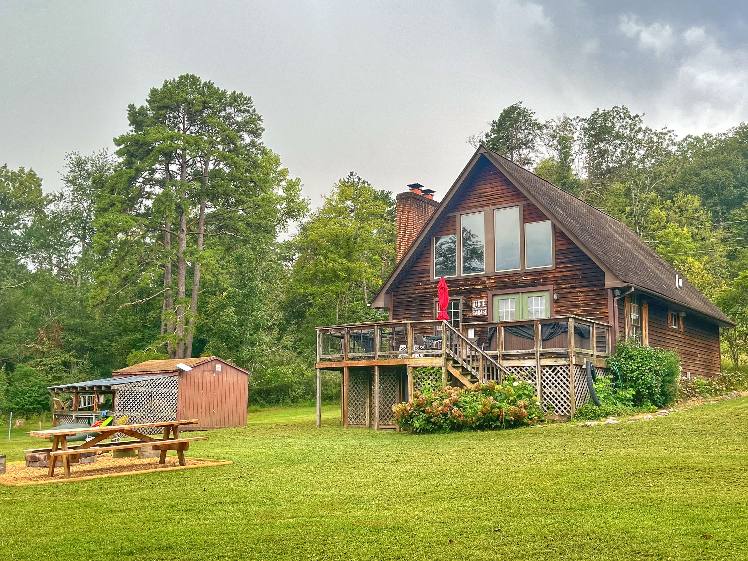 A cabin with a deck, a picnic table, and a small shed.