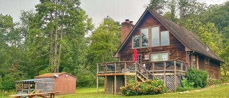 A cabin with a deck, a picnic table, and a small shed.
