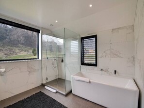 Een moderne badkamer met een douchecabine van glas, een witte badkuip en uitzicht op een bergachtig landschap.