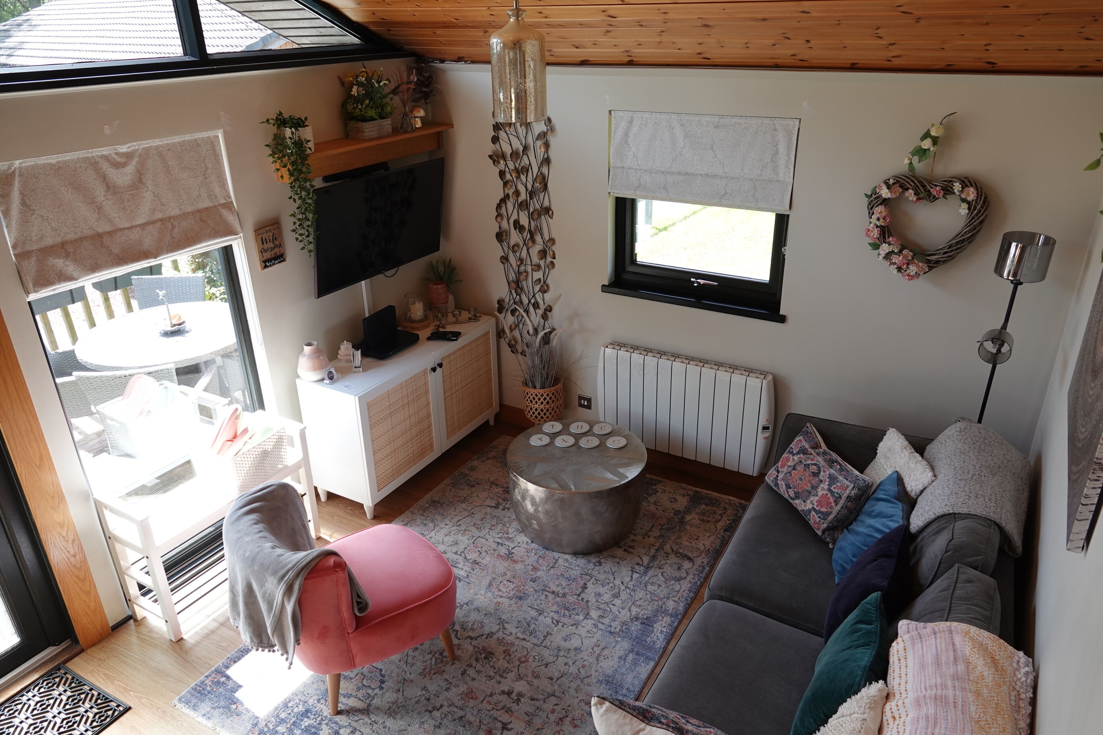 A cozy living room with a sofa, a coffee table, a pink chair, a TV, and a window with a view.