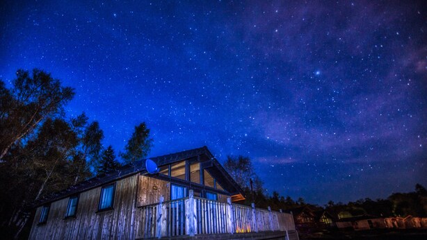 A rustic wooden cabin with a satellite dish, surrounded by trees under a starry night sky. - Boutique, 3 bedroom lodge in the heart of Northumberland with private hot tub (Newcastle upon Tyne)